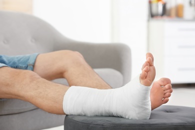 Young man with broken leg in cast sitting on sofa at home