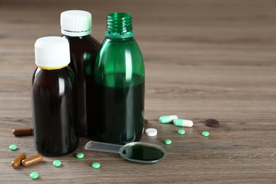 Bottles of cough syrup, dosing spoon and pills on wooden table