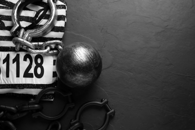 Prisoner ball with chain and jail clothes on black table, flat lay. Space for text