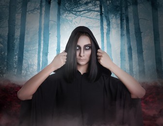 Image of Witch wearing black mantle in foggy forest. Scary fantasy character