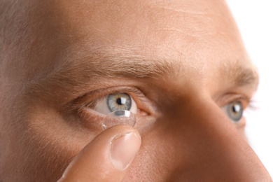 Young man putting contact lens into his eye, closeup