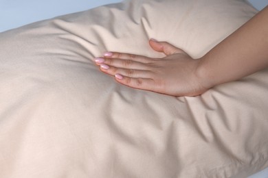 Photo of Woman touching soft beige pillow on bed, closeup
