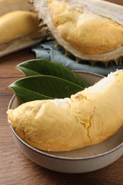Photo of Bowl with piece of fresh ripe durian and leaves on wooden table, closeup