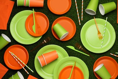 Photo of Disposable tableware on green artificial grass, flat lay