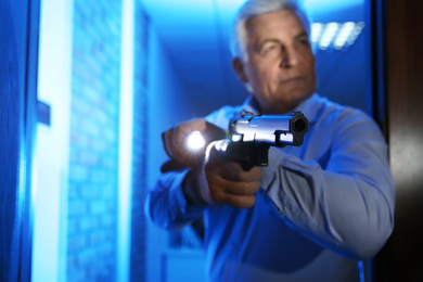 Professional security guard with gun checking dark room, focus on hand
