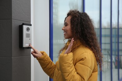 Young African-American woman ringing intercom while waving to camera near building entrance