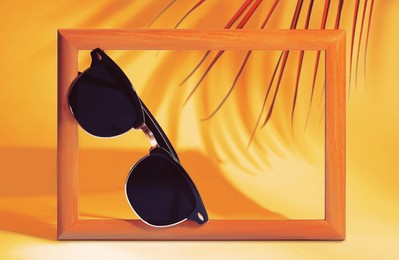 Image of Stylish sunglasses near photo frame on orange background