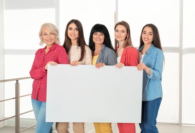 Group of ladies with empty poster near window indoors, space for text. Women power concept
