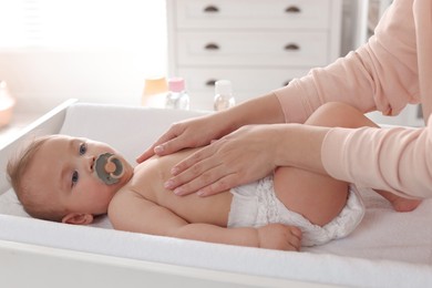 Mother massaging her cute baby with oil on changing table at home, closeup