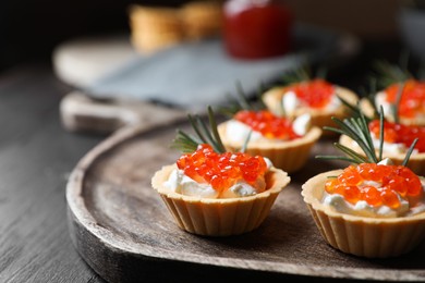 Photo of Delicious tartlets with red caviar and cream cheese served on wooden table, closeup