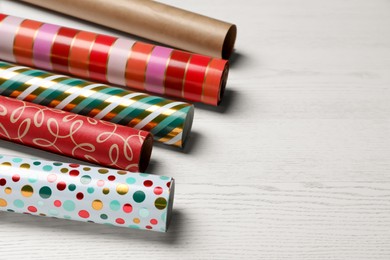 Different colorful wrapping paper rolls on white wooden table. Space for text