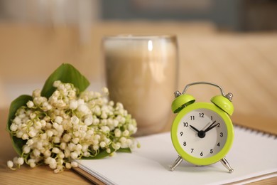 Cup of aromatic morning coffee, notepad, alarm clock and flowers on wooden table in cafe
