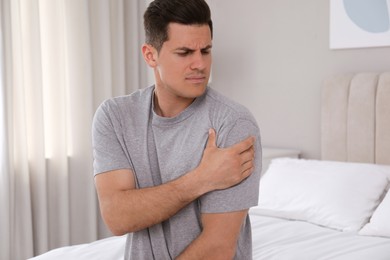 Man suffering from shoulder pain on bed at home