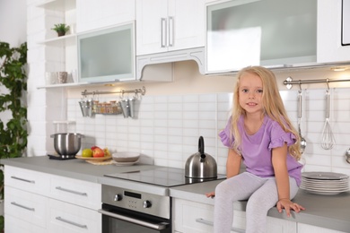 Photo of Cute little girl near oven in kitchen