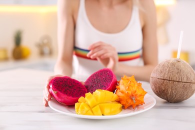 Photo of Young woman with fresh exotic fruits at table in kitchen, closeup