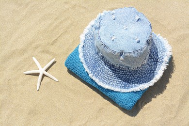 Stylish denim hat, towel and starfish on sand outdoors, above view. Beach accessories