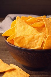 Photo of Tortilla chips (nachos) in bowl on wooden table against dark background, closeup
