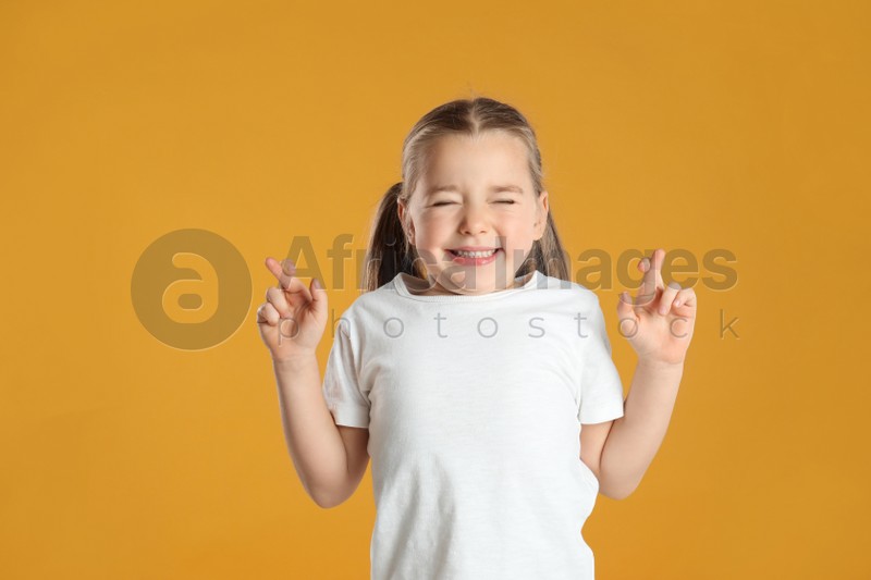Child with crossed fingers on yellow background. Superstition concept