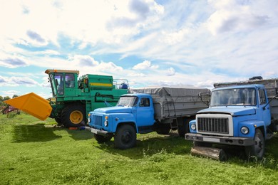 Modern combine harvester and old trucks on green lawn with fresh grass