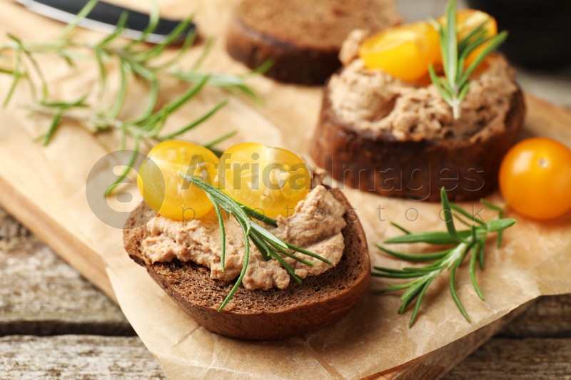 Slices of bread with delicious pate, tomatoes and rosemary on wooden table, closeup