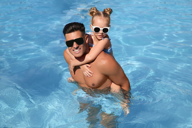 Happy man and his daughter in outdoor swimming pool on sunny summer day