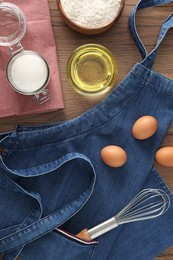Photo of Denim apron with kitchen tool and different ingredients on wooden table, flat lay