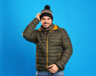 Happy young man in warm clothes on blue background. Winter vacation