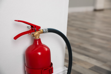 Fire extinguisher near white wall indoors, closeup. Space for text