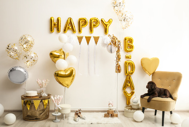 Chocolate Labrador Retriever and phrase HAPPY BIRTHDAY made of golden balloon letters in decorated room