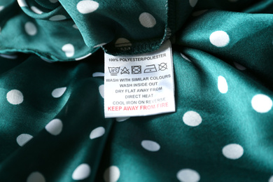 Clothing label with care instructions and content information on green polka dot garment, closeup