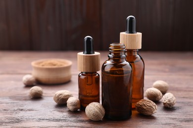 Photo of Bottles of nutmeg oil and nuts on wooden table