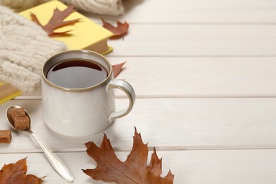 Cup of hot tea, sweater and autumn leaves on white wooden table, space for text