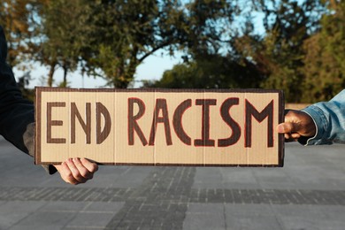 Men holding sign with phrase End Racism outdoors, closeup