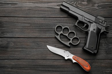 Brass knuckles, gun and knife on black wooden background, flat lay. Space for text