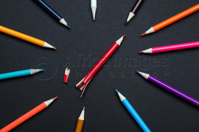 Whole colorful pencils and broken one on black background, flat lay. Bullying concept