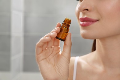 Photo of Young woman smelling essential oil indoors, closeup