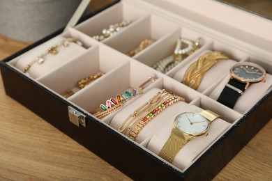 Elegant jewelry box with beautiful bijouterie and expensive wristwatches on wooden table, closeup