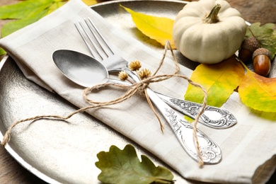 Autumn place setting with pumpkin and fallen leaves on table, closeup