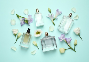 Flat lay composition with different perfume bottles and flowers on cyan background