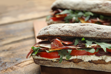 Delicious sandwiches with fresh vegetables and prosciutto on wooden table, closeup