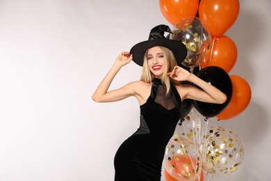 Beautiful woman in witch costume with balloons on white background, space for text. Halloween party