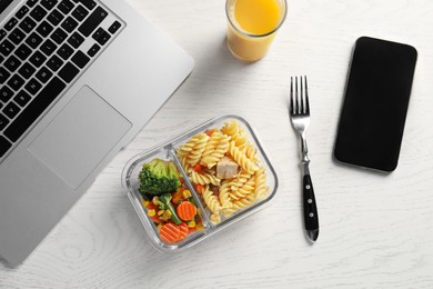 Photo of Container with tasty food, glass of juice, laptop, fork and smartphone on white wooden table, flat lay. Business lunch