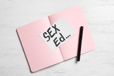 Notebook with text "SEX ED..." on white wooden background, top view