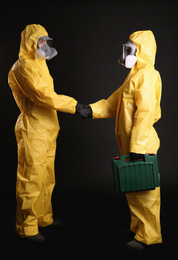 Man and woman in chemical protective suits shaking hands on black background. Virus research