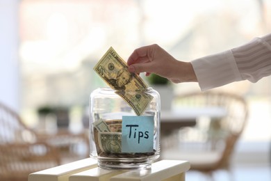 Woman putting tips into glass jar at table, closeup