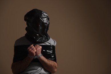 Photo of Tied man wrapped in black plastic bag on his head against dark background, space for text. Hostage taking