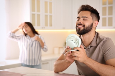 Man with portable fan enjoying cool air while his girlfriend suffering from heat at home