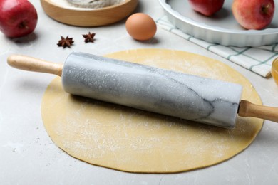 Rolling pin, raw dough and ingredients on light grey table. Baking apple pie