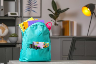 Turquoise backpack with different school stationery on table indoors, space for text