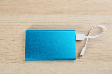 Modern portable charger with cable on wooden background, top view
